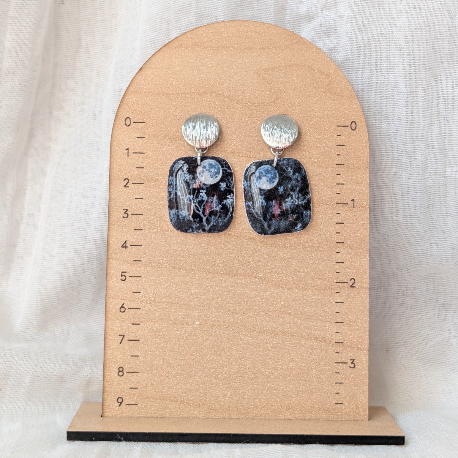 Blue moon square earrings with silver posts displayed beside a ruler