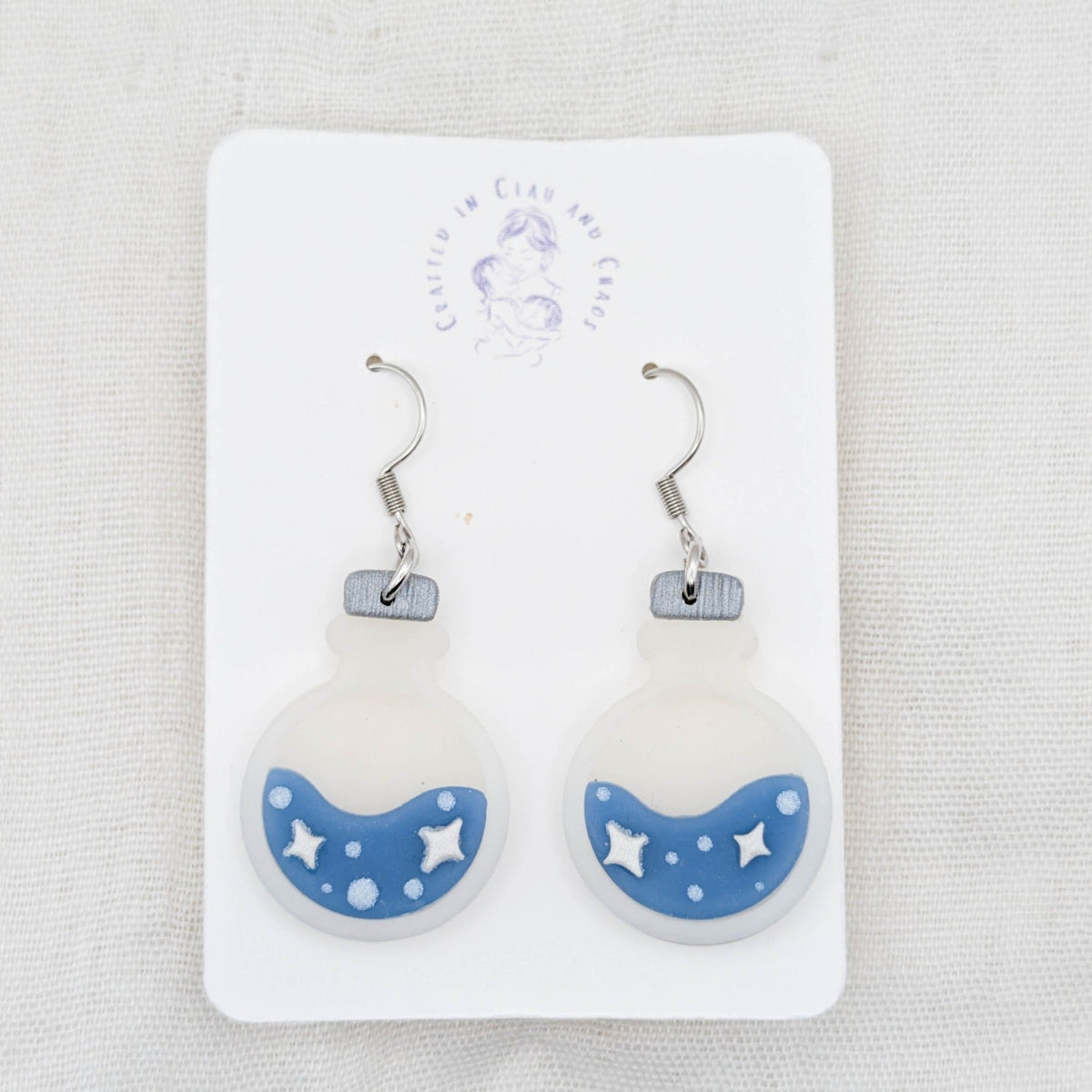Blue translucent potion bottle earrings with painted white stars and bubbles on surgical-grade stainless steel hooks