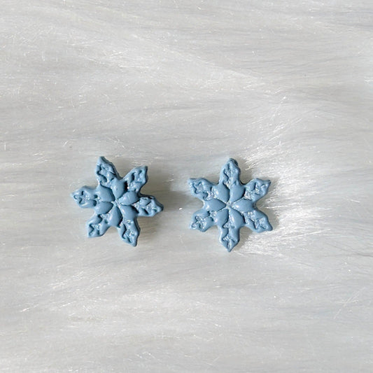 Close-up of handmade icy blue polymer clay snowflake stud earrings with detailed texture
