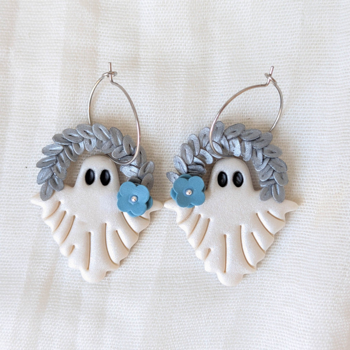 Pearlescent botanical ghost earrings with silver leaf crowns, blue flowers, and surgical-grade stainless steel hoops