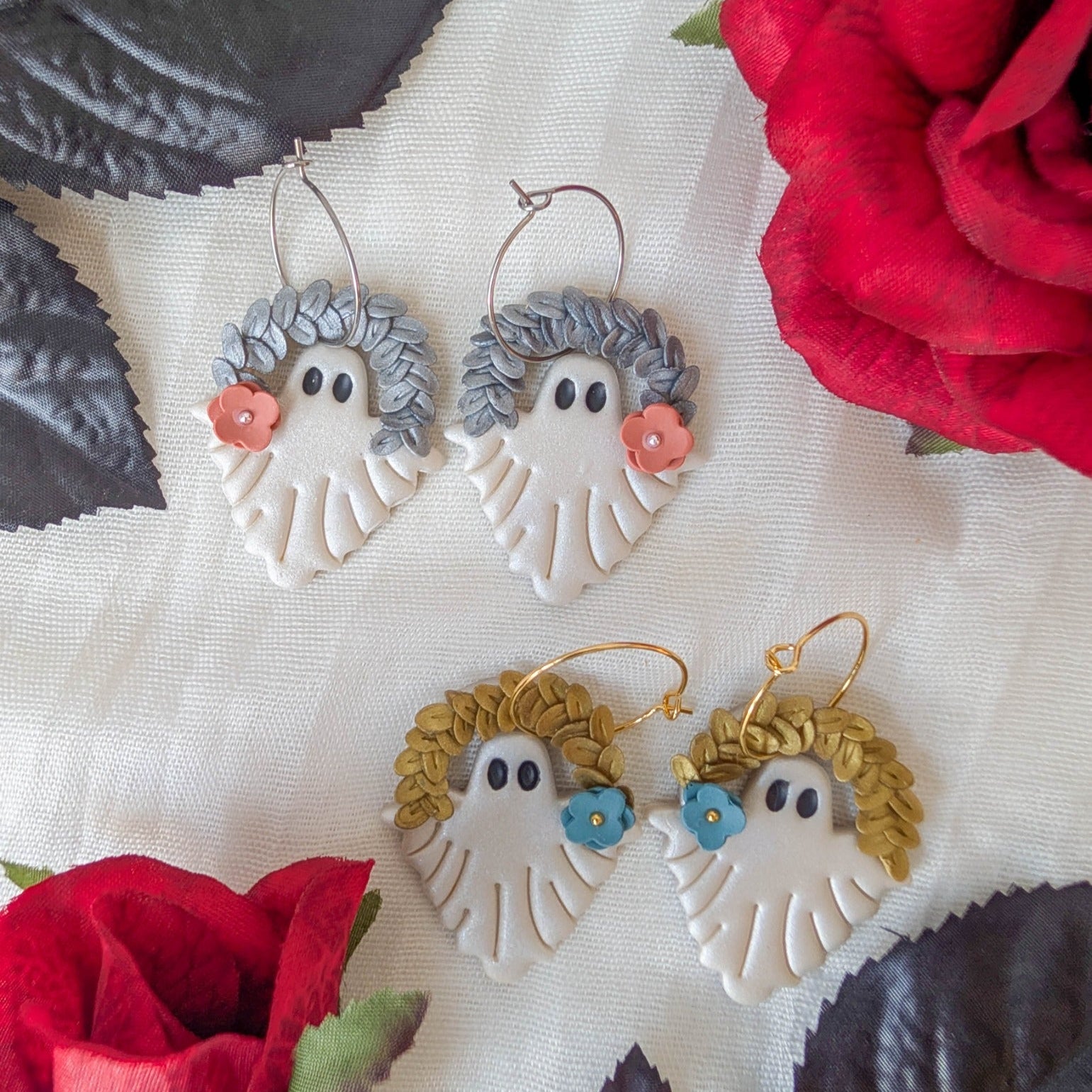 Gold and silver botanical leaf ghost earrings with coral and blue flowers styled with red roses and black leaves