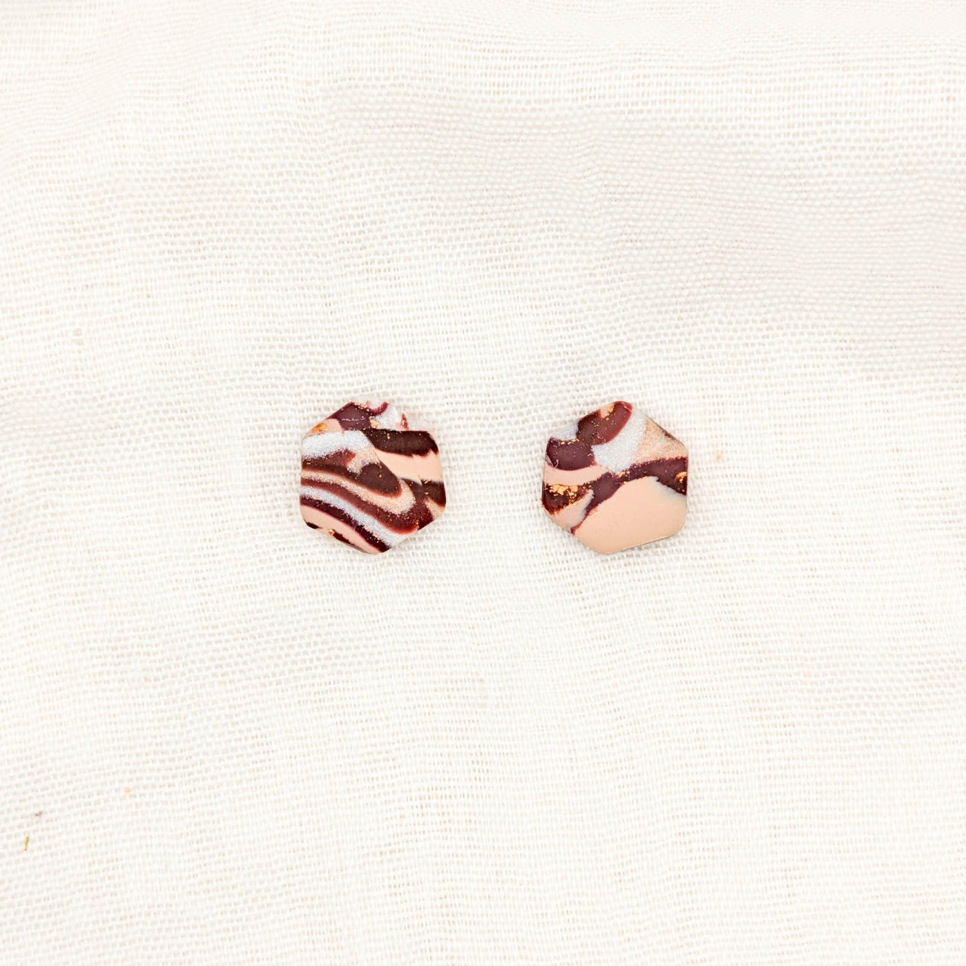 Close-up of geometric hexagon polymer clay stud earrings with brown, cream, and copper marbling