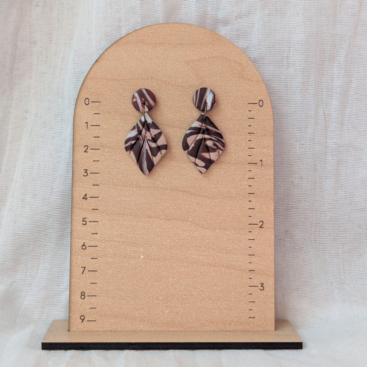 Brown marble leaf dangle earrings displayed beside a ruler