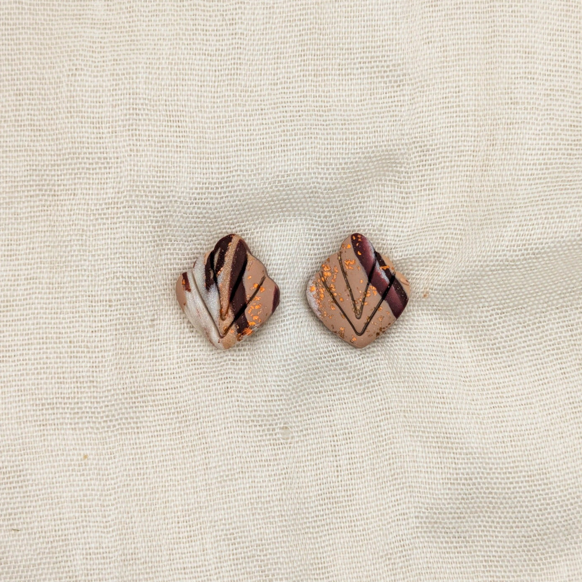 Close-up of brown marbled leaf-shaped polymer clay stud earrings with carved veins and copper accents