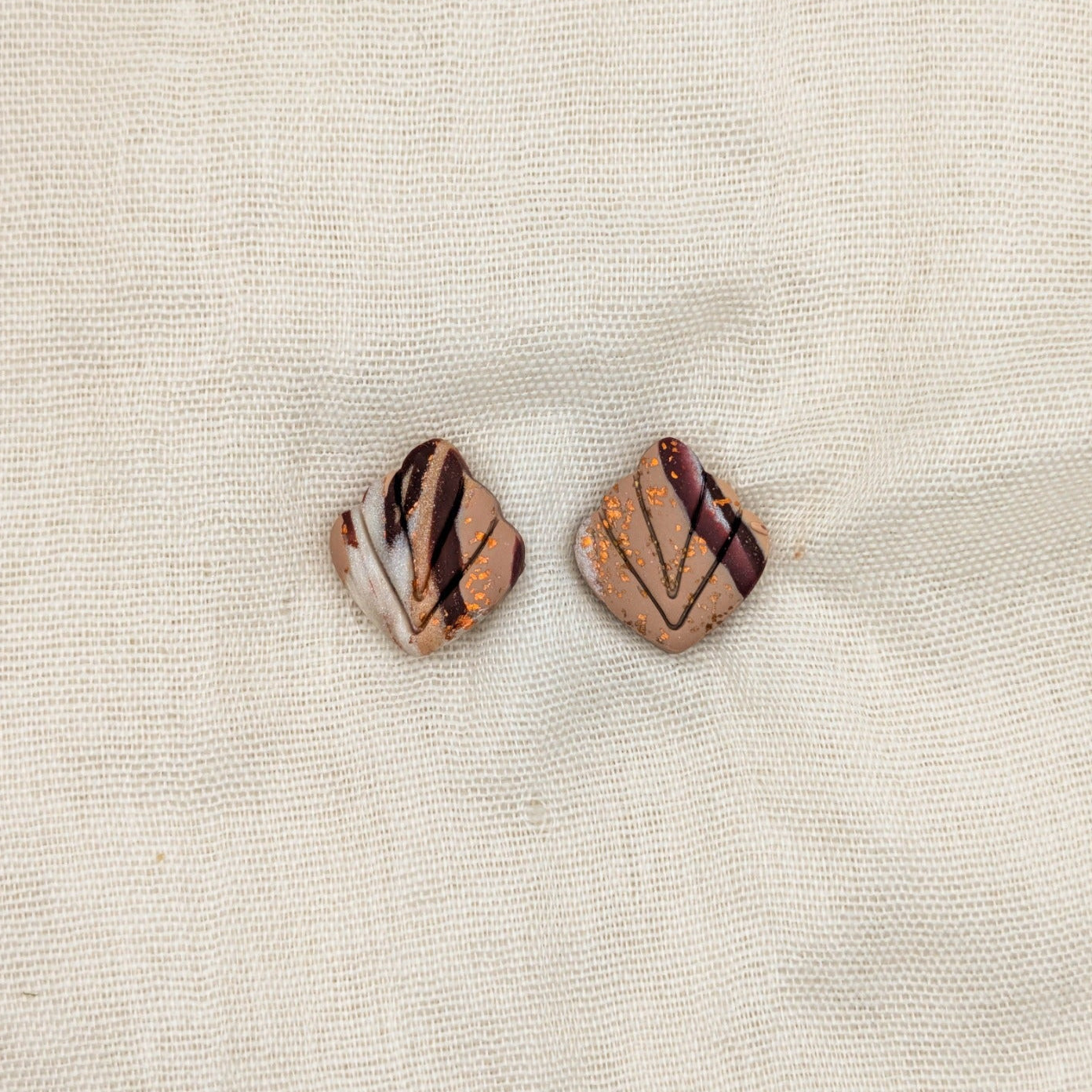 Close-up of brown marbled leaf-shaped polymer clay stud earrings with carved veins and copper accents