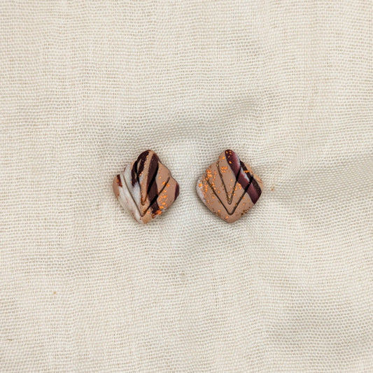 Close-up of brown marbled leaf-shaped polymer clay stud earrings with carved veins and copper accents