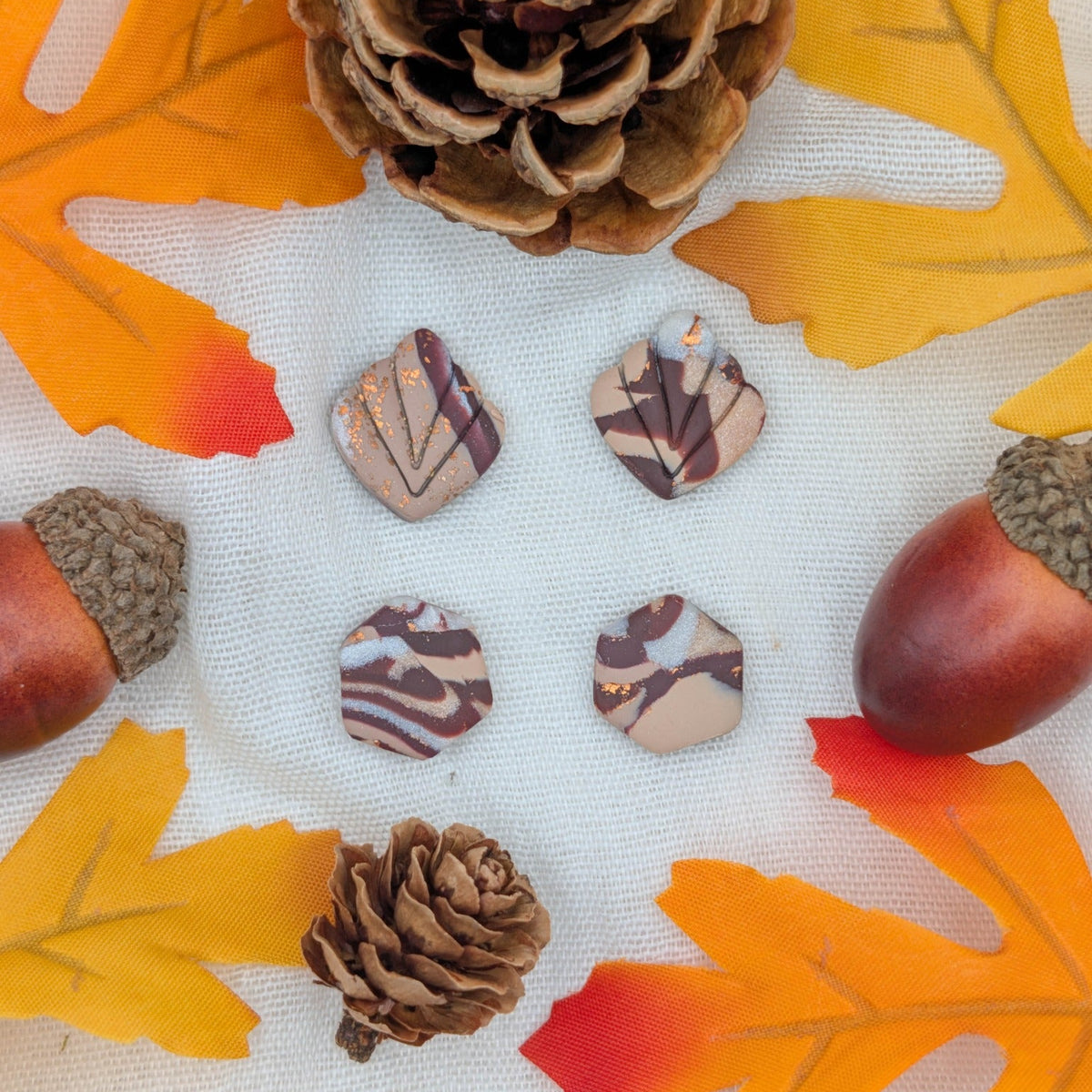 Brown marble leaf and hexagon polymer clay stud earrings with copper accents styled with autumn leaves, acorns, and pinecones