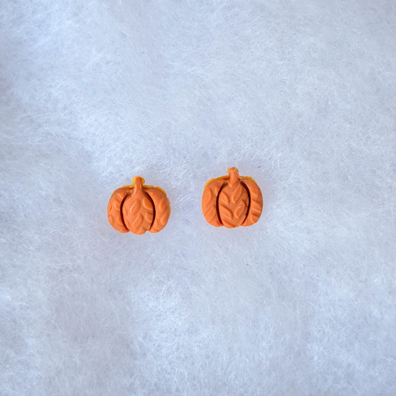 Tiny burnt orange pumpkin stud earrings with a raised knitted texture