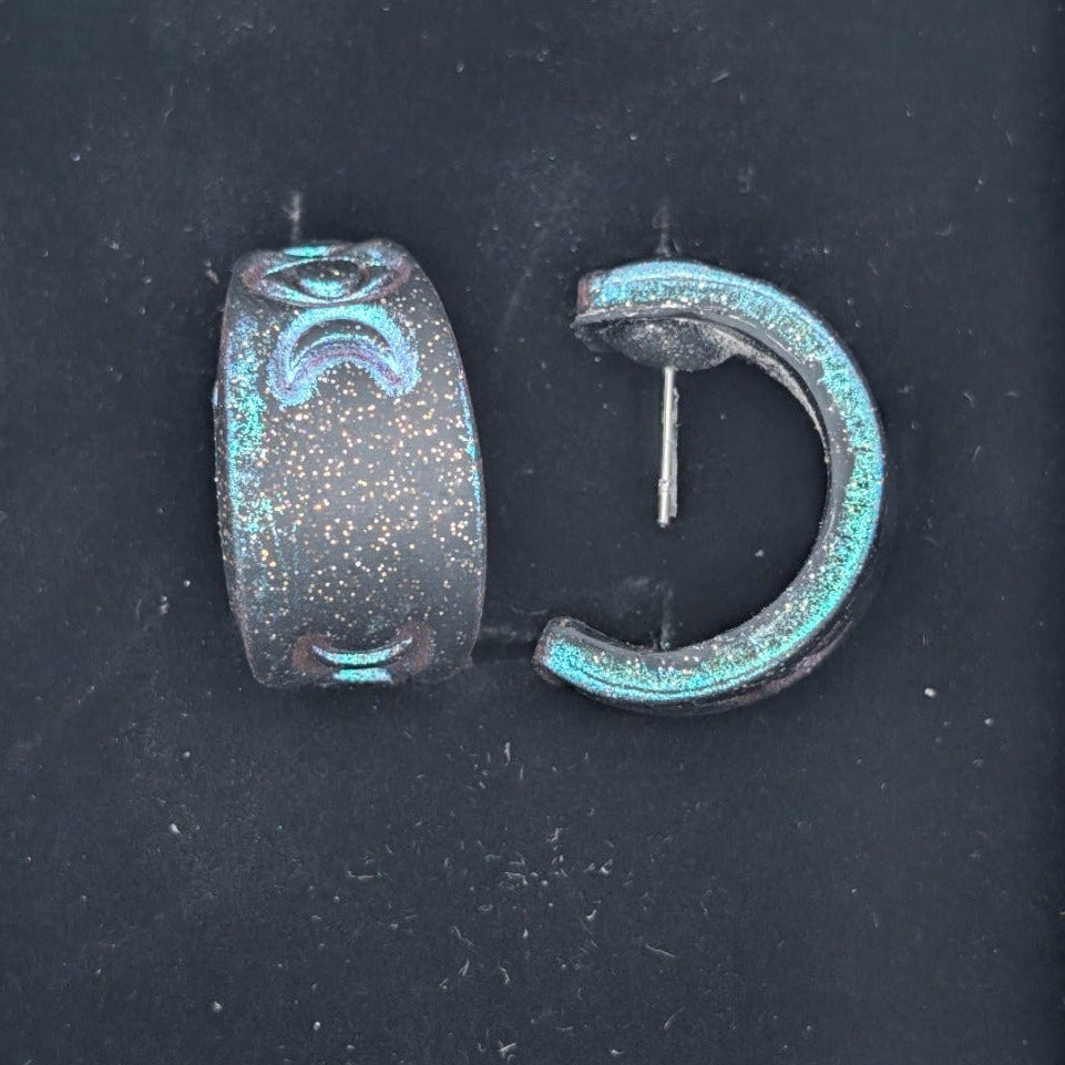 Close-up of color-shifting celestial huggie earrings with moon phase details and surgical stainless steel posts