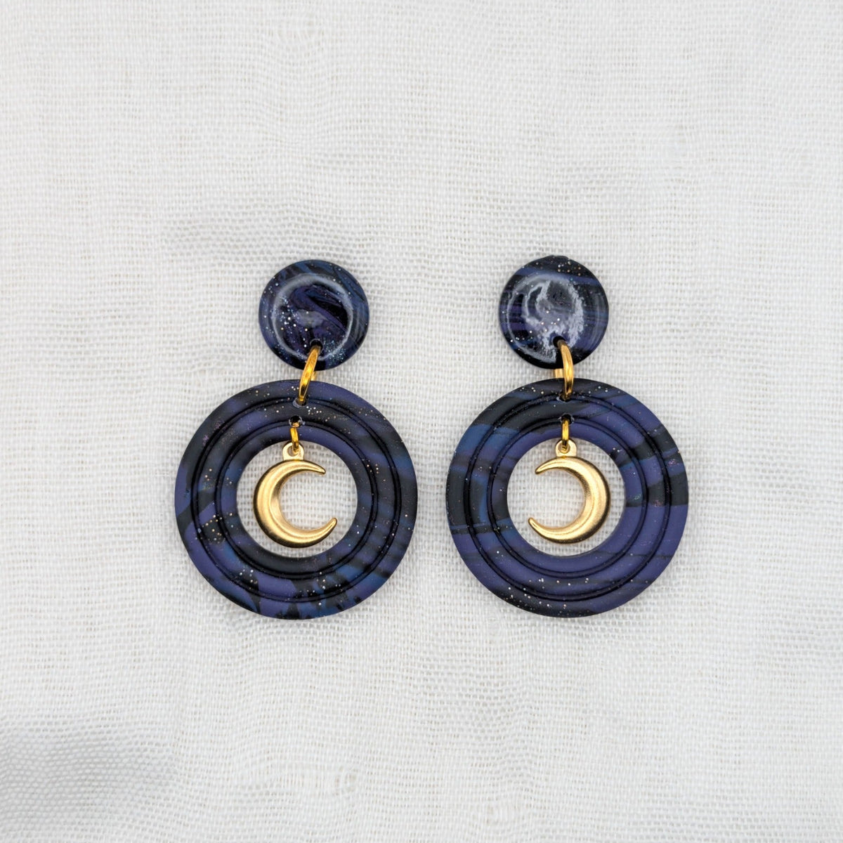 Gold-toned celestial crescent moon earrings with deep purple, midnight blue, and black marbled double-circle drops