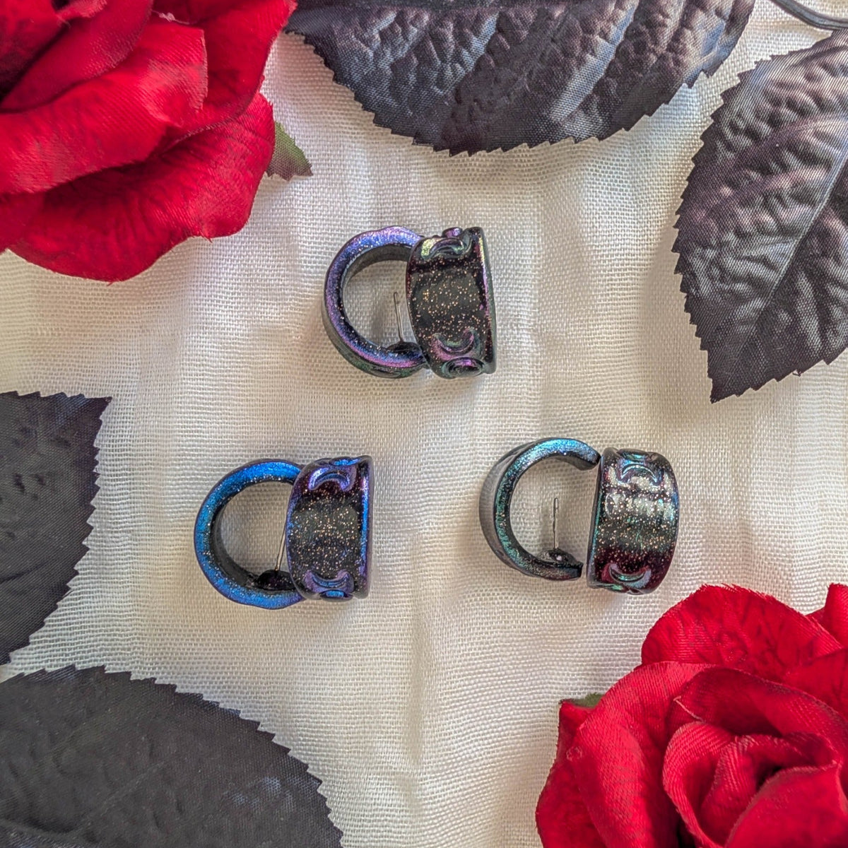 Three pairs of sparkly celestial polymer clay huggie earrings in Galaxy, Blue, and Purple with red roses