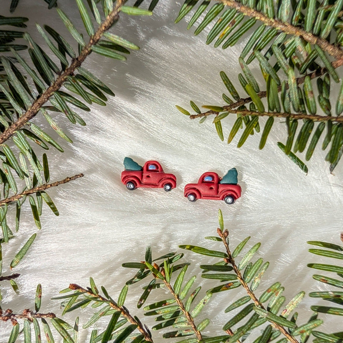 Handmade red Christmas tree truck stud earrings styled with evergreen branches