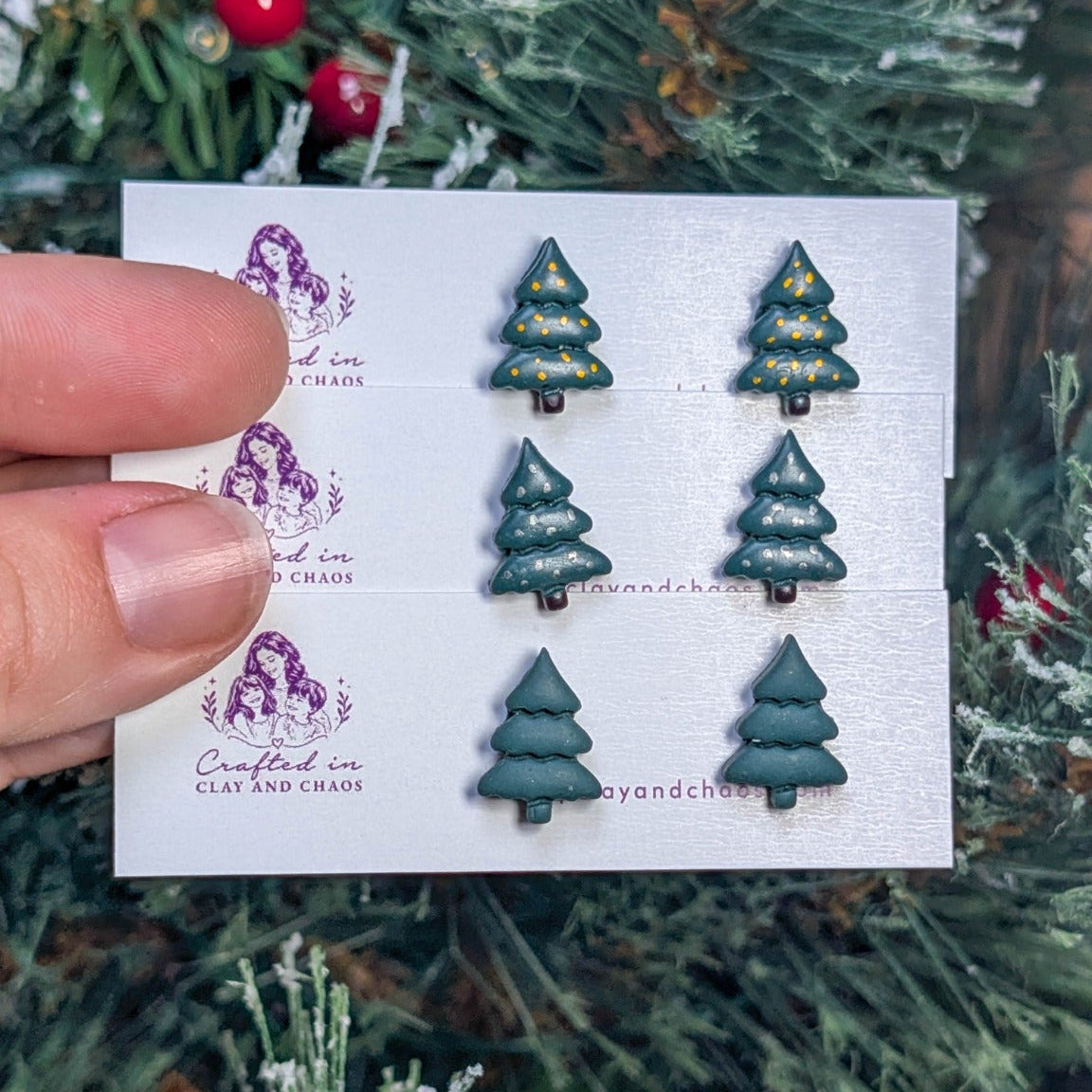 Three styles of green Christmas tree stud earrings displayed against holiday greenery