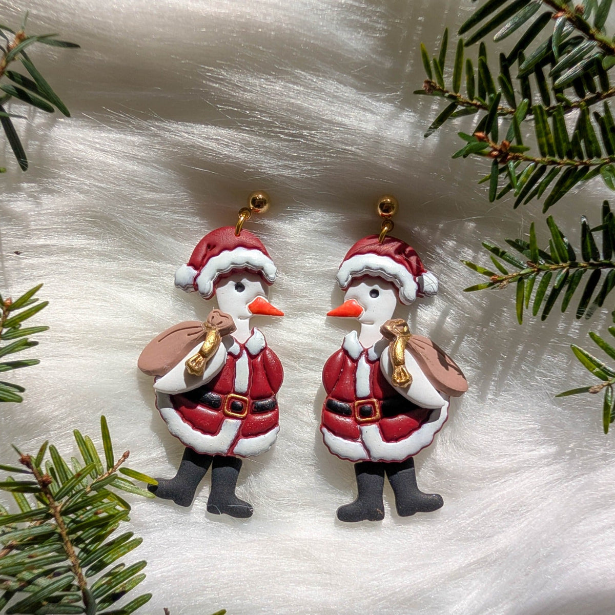 Pair of whimsical Santa Goose earrings styled with evergreen branches
