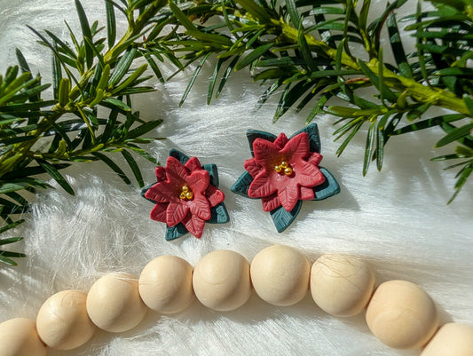Red poinsettia stud earrings styled on white faux fur with evergreen branches