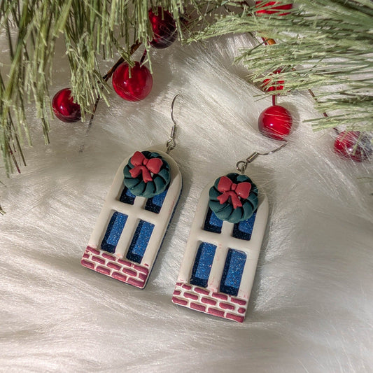 Christmas window earrings with wreaths and red bows styled among evergreen branches.