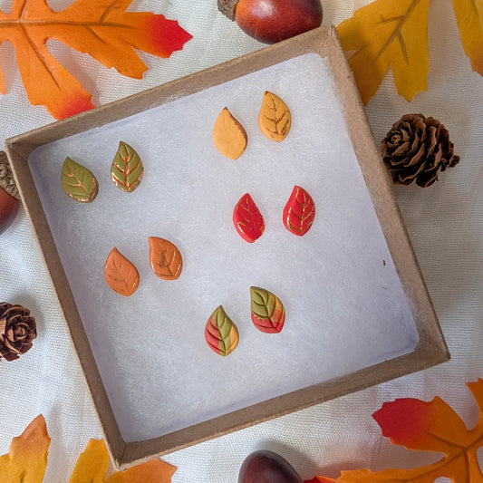 Red, green, orange, yellow, and marbled autumn leaf stud earrings with copper accents in a fall display