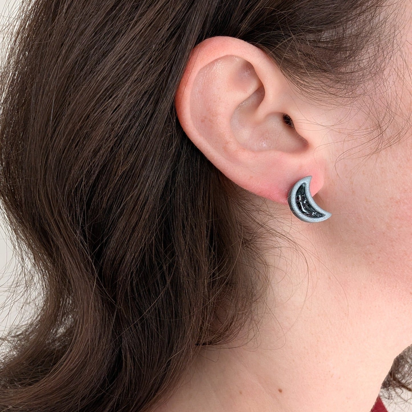 Silver crescent moon stud earring worn on ear
