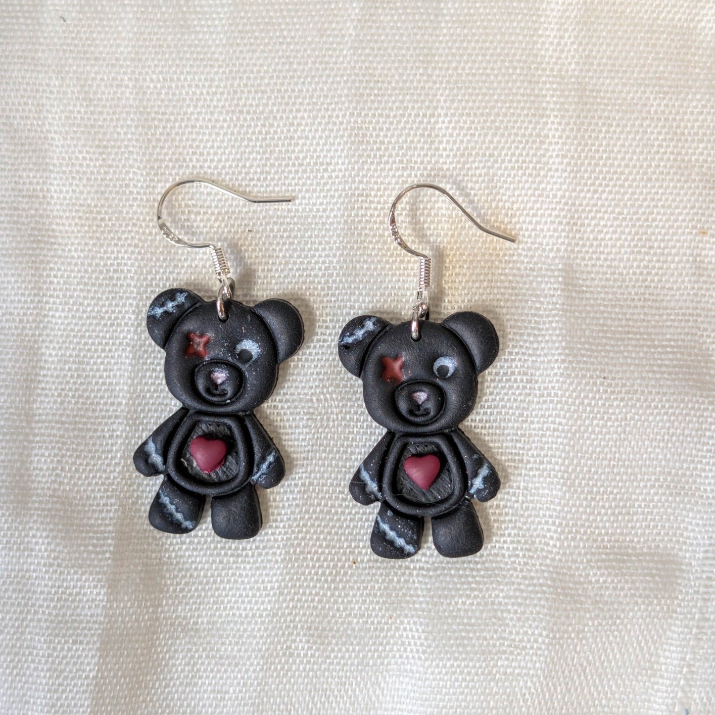Close-up of handmade charcoal Franken bear Halloween earrings with stitched details and exposed red hearts