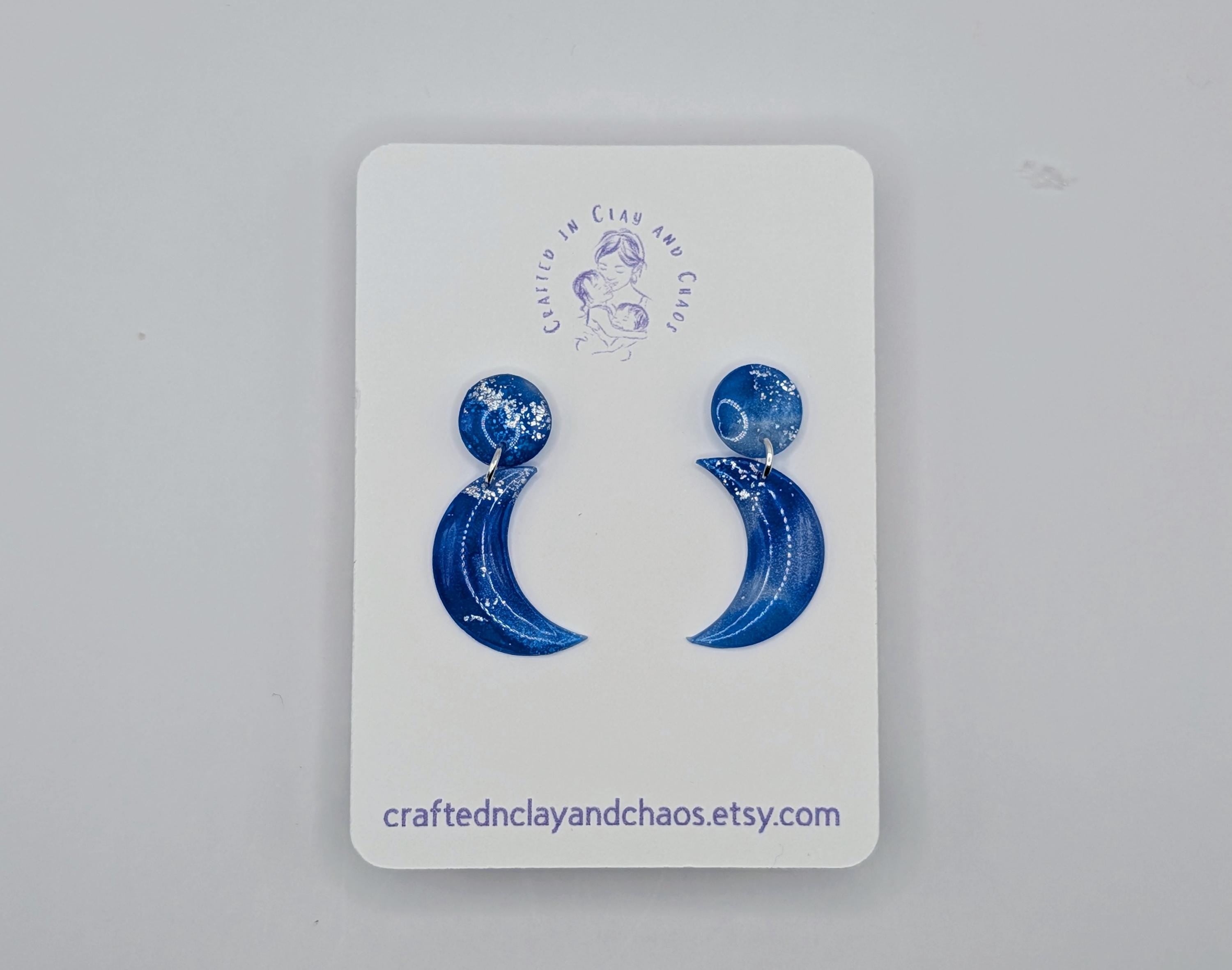 Blue crescent moon earrings on a white card with branding.