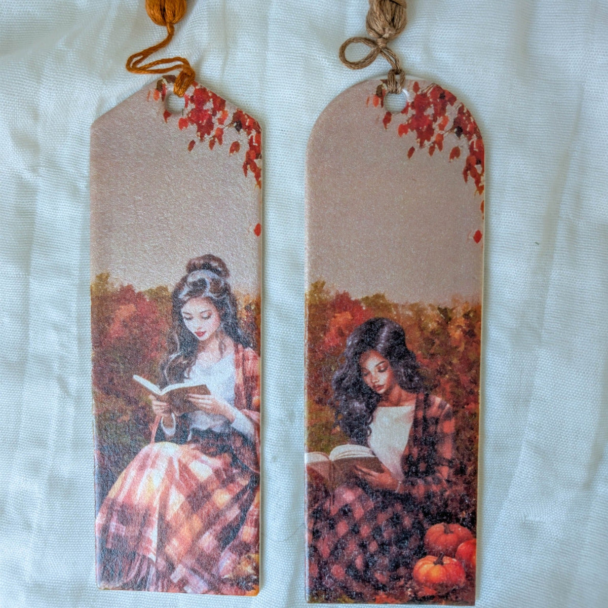 Two handmade fall reading bookmarks with autumn foliage, reader illustrations, pumpkins, and orange and taupe tassels