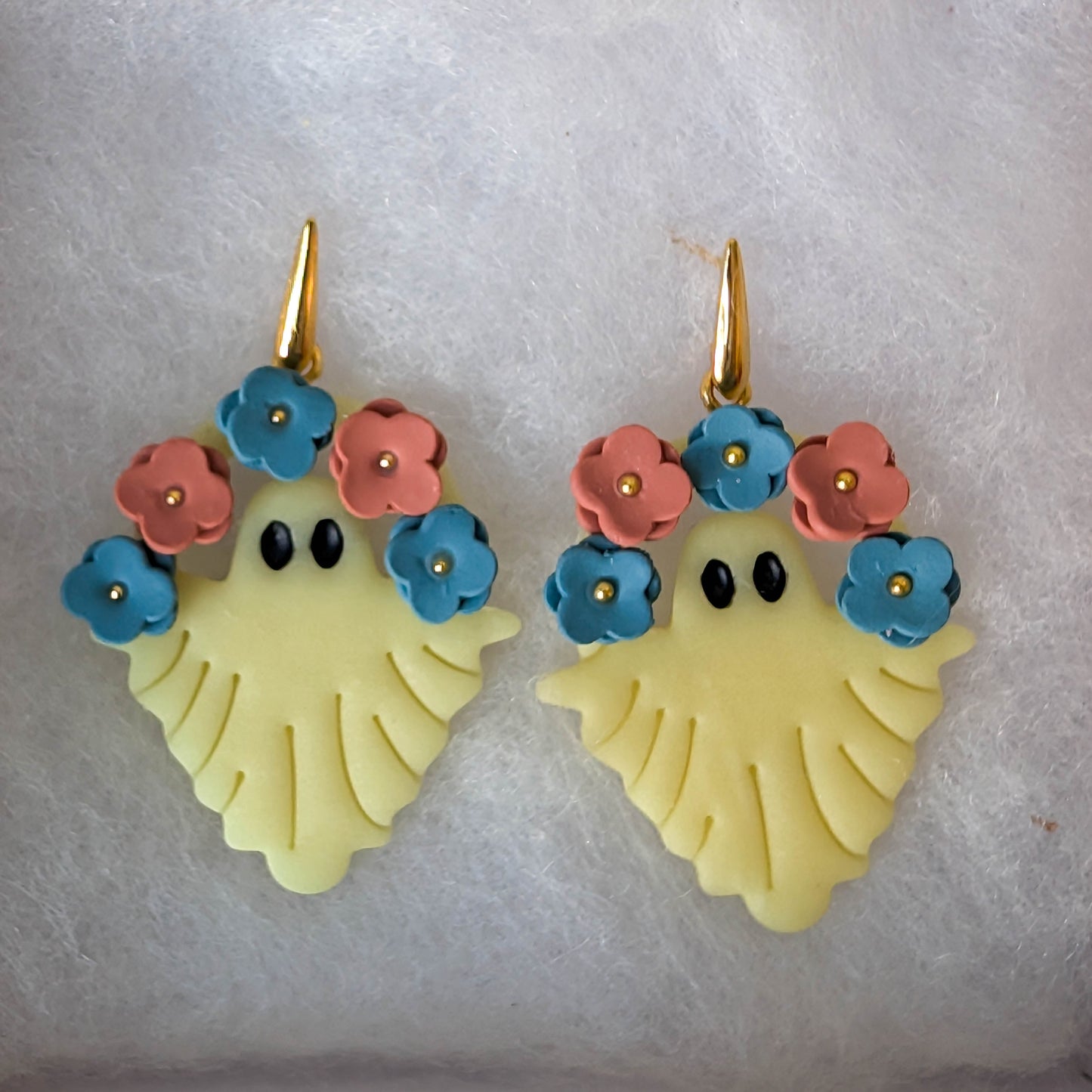 Ivory glow-in-the-dark ghost earrings with blue and terracotta flower crowns and gold hooks