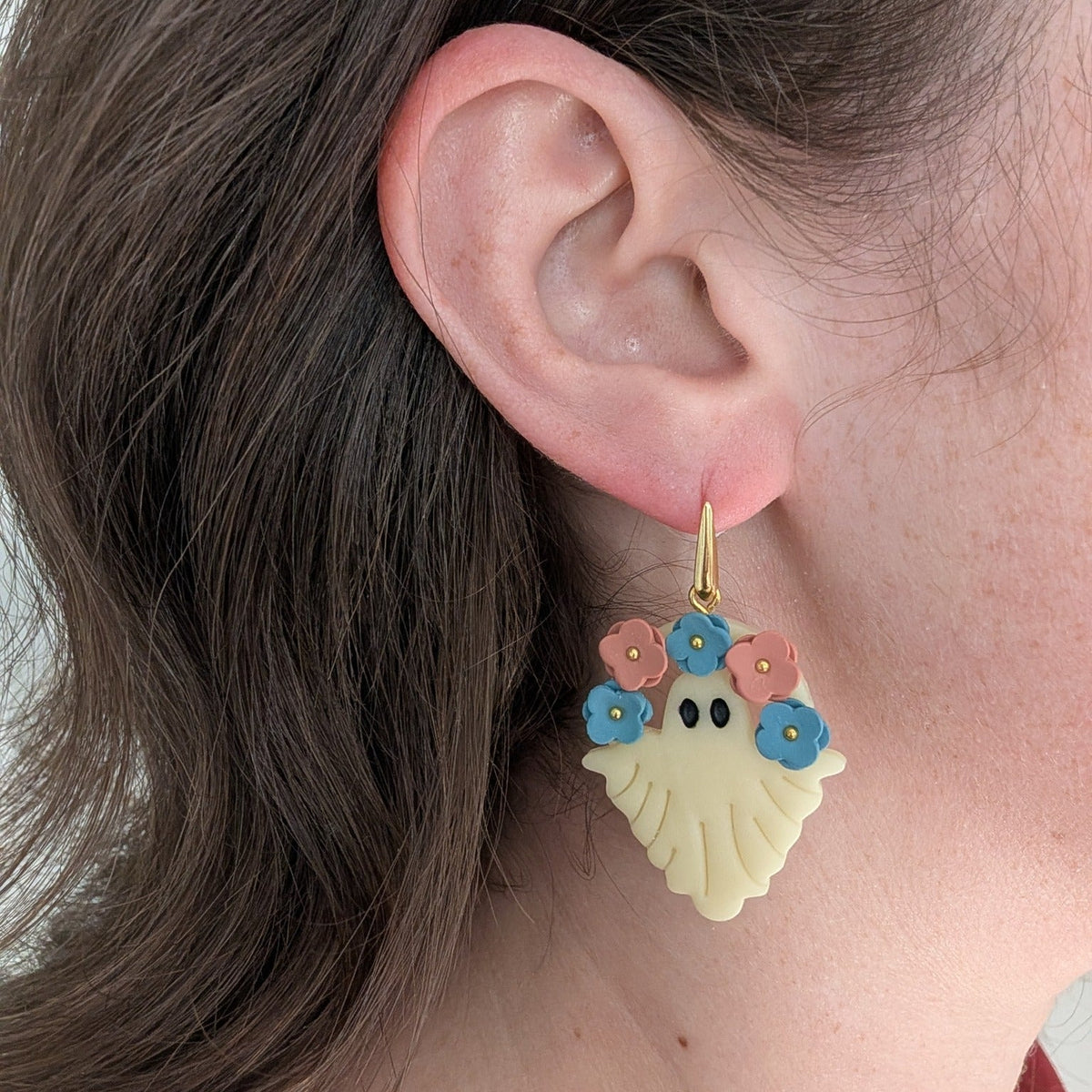 Glow-in-the-dark floral ghost earring with blue and terracotta flowers worn on ear