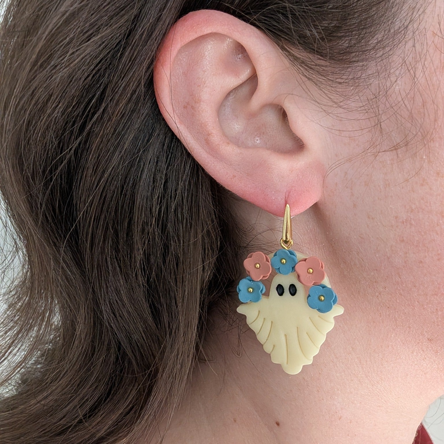 Glow-in-the-dark floral ghost earring with blue and terracotta flowers worn on ear