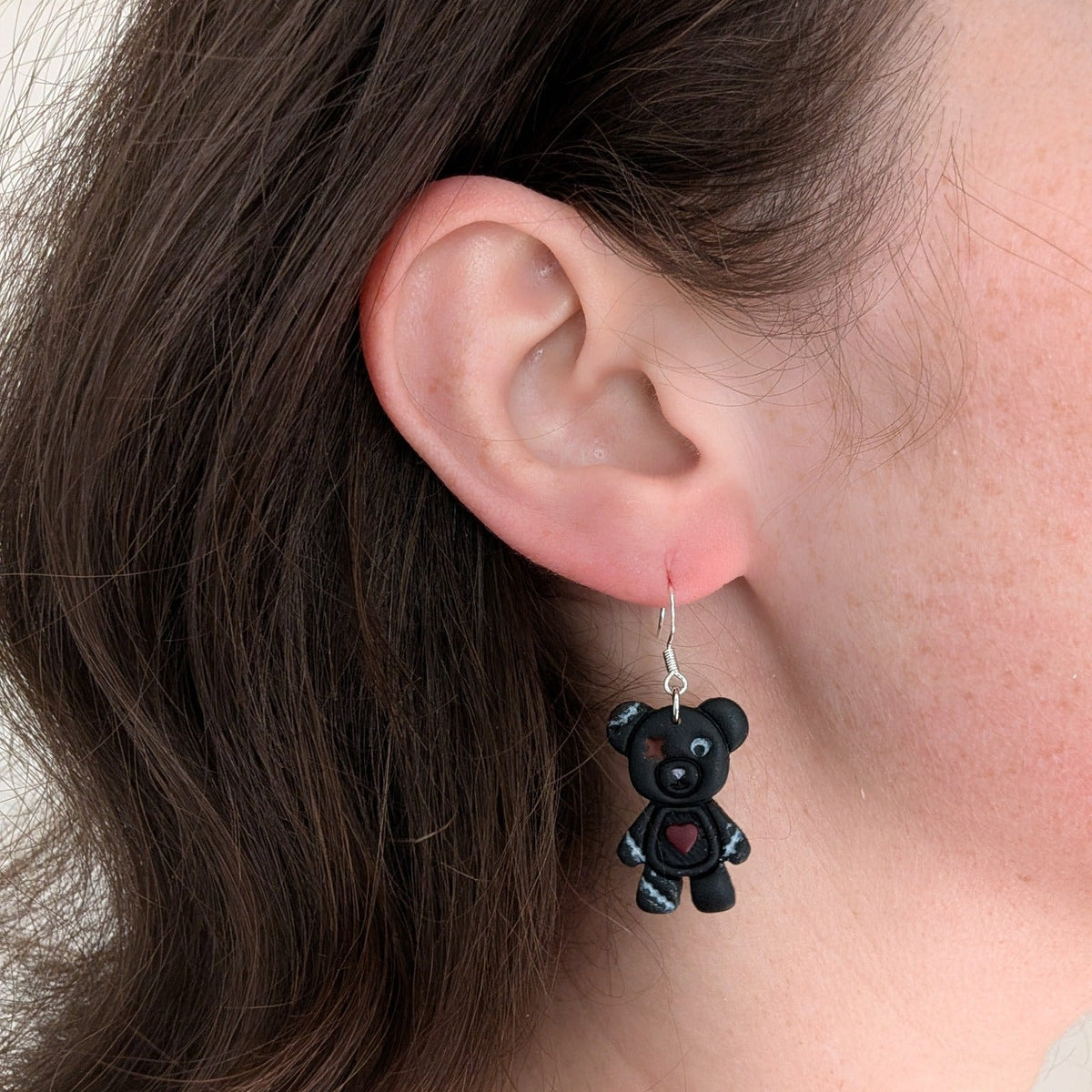 Charcoal Frankenstein teddy bear earring with stitched details and exposed heart worn on ear
