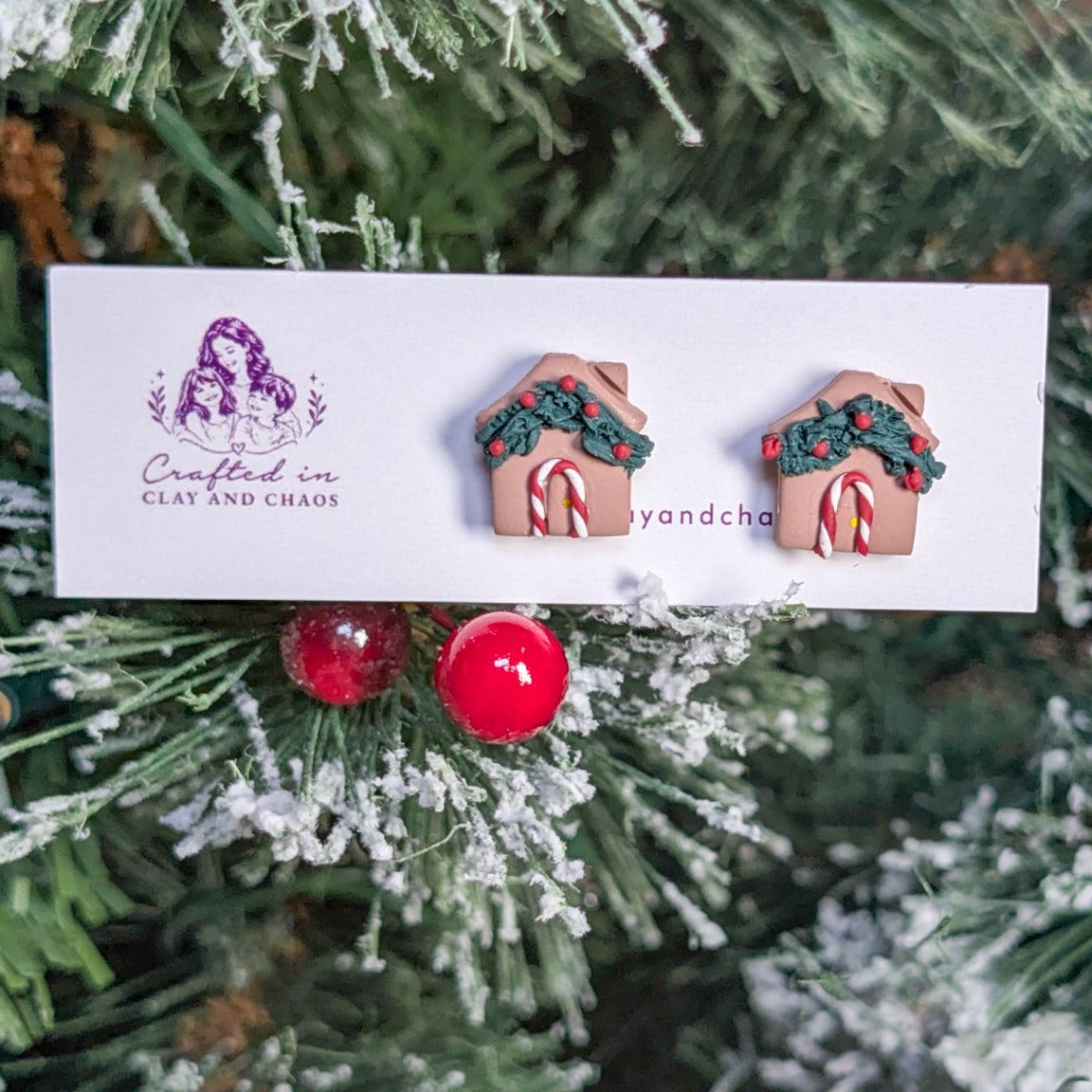 Pair of gingerbread house stud earrings displayed against snowy Christmas greenery