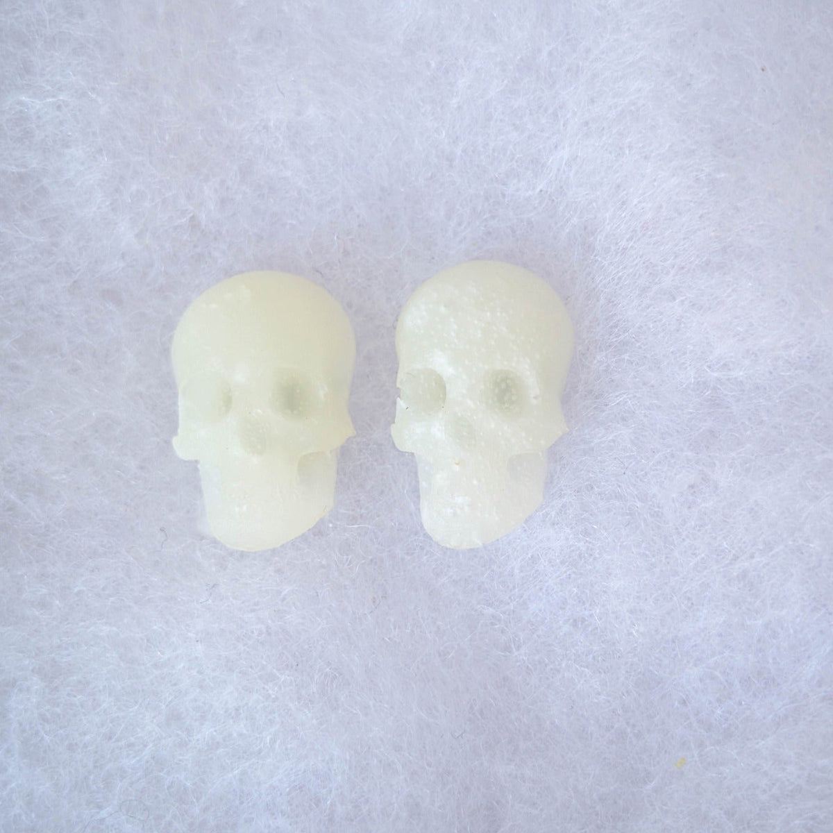 Translucent glow-in-the-dark skull stud earrings shown in daylight