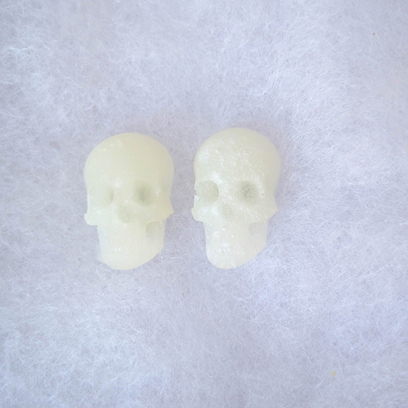 Translucent glow-in-the-dark skull stud earrings shown in daylight