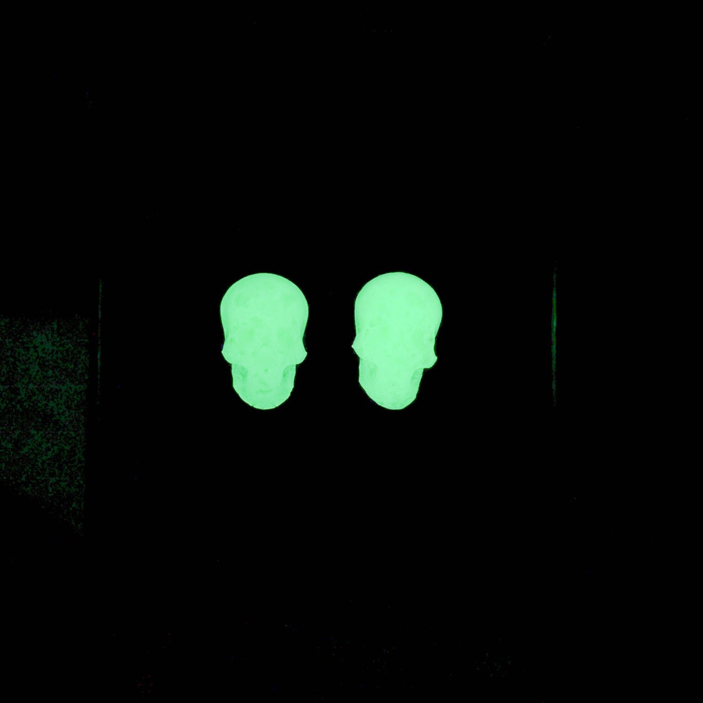 Skull stud earrings glowing vivid green in darkness