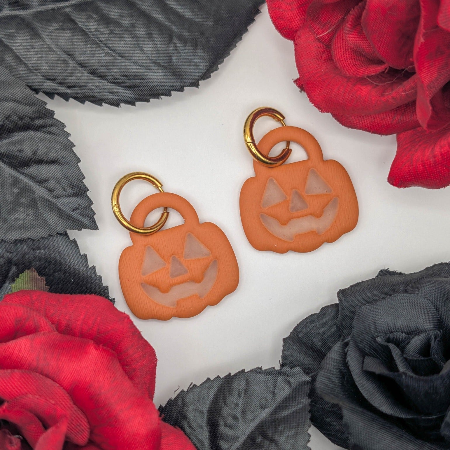 Glow-in-the-dark trick-or-treat pumpkin earrings styled with red roses and black leaves