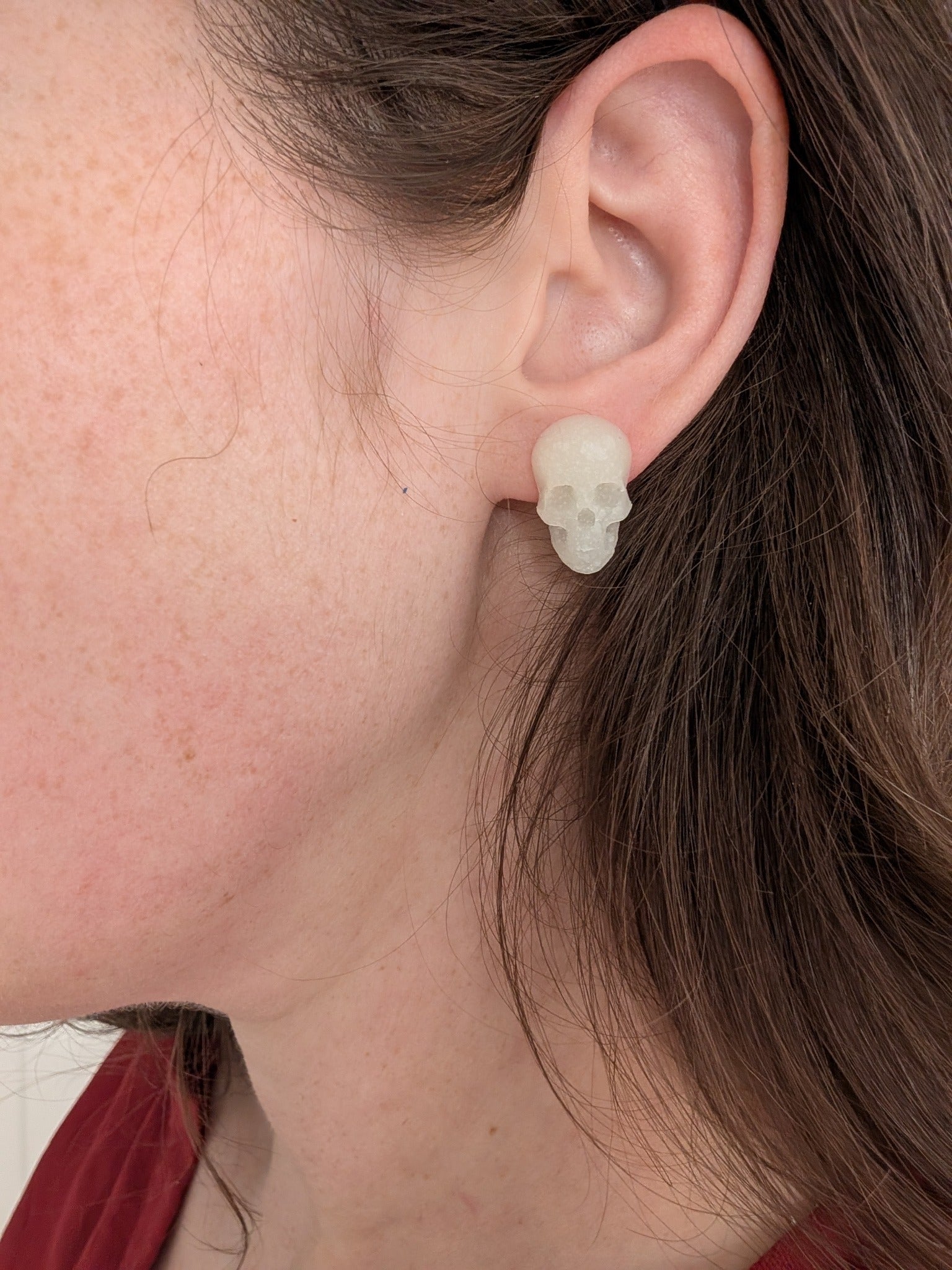 Glow-in-the-dark skull stud earring worn on ear