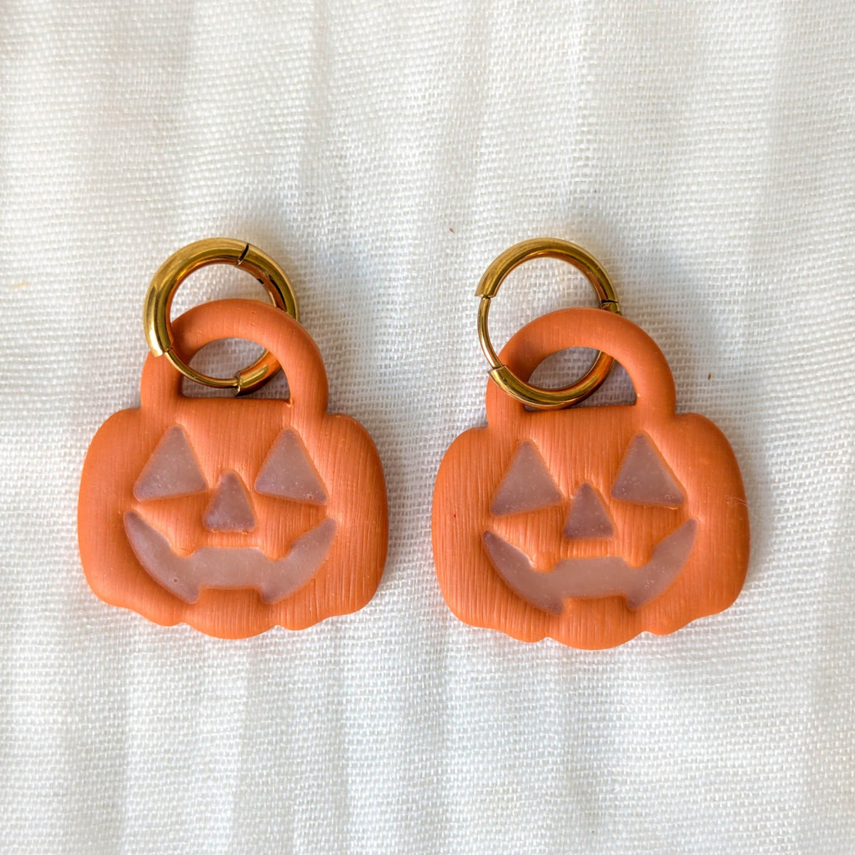 Orange trick-or-treat pumpkin earrings with glow-in-the-dark jack-o-lantern faces and gold-tone huggie hoops