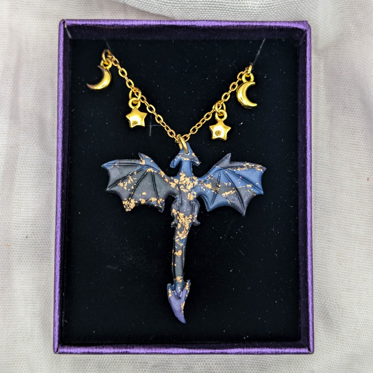 Gold-tone dragon necklace with marbled pendant and moon and star chain charms