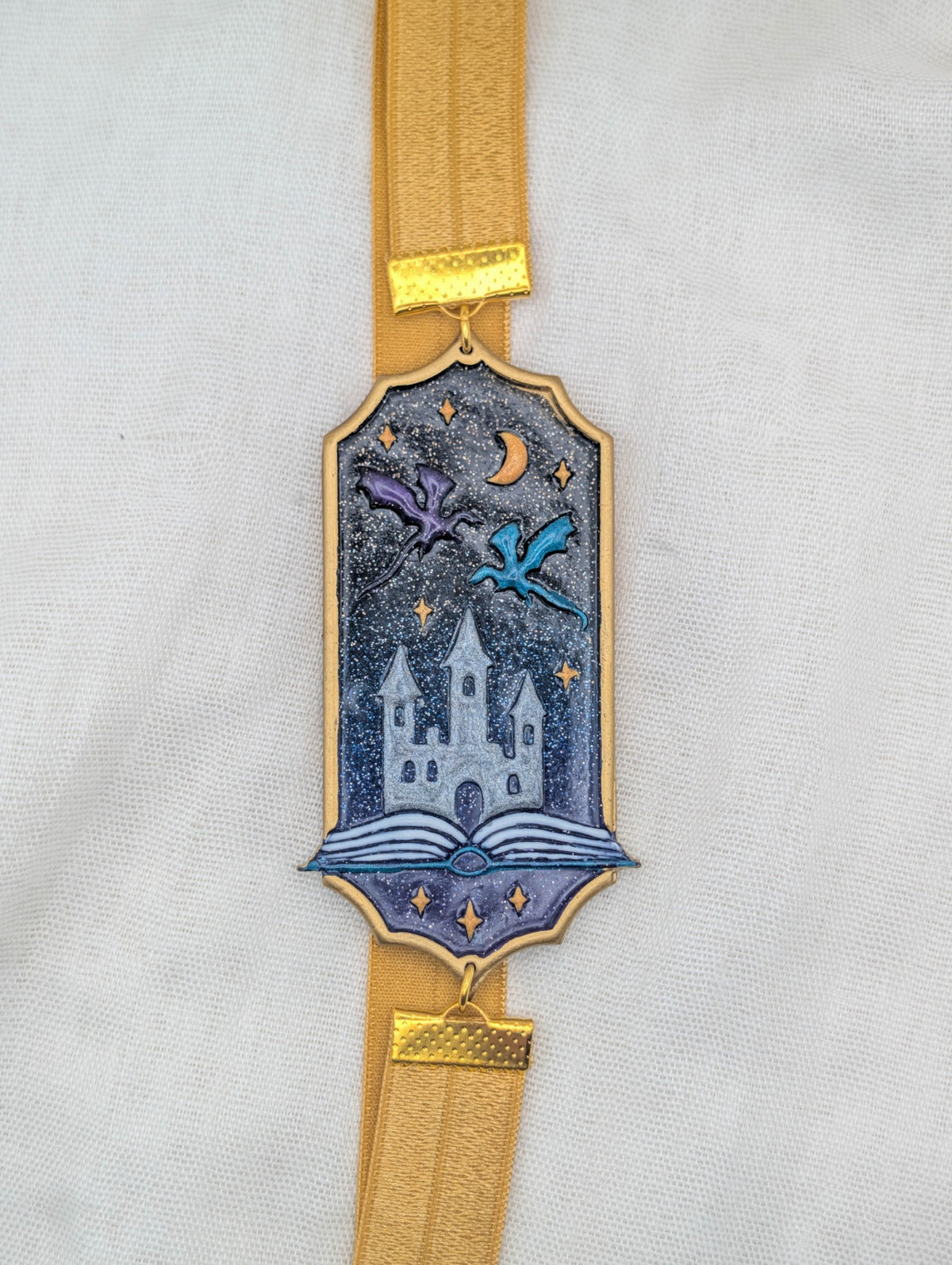 Gold framed fantasy polymer clay wrap-around bookmark with purple and blue dragons over a castle and glittering midnight sky