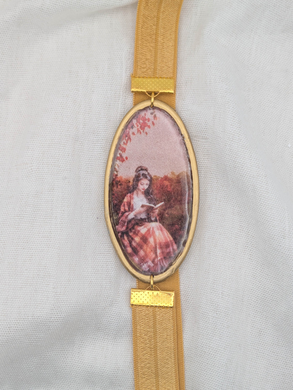 Gold framed fall polymer clay wrap-around bookmark showing a woman reading in a plaid skirt among autumn leaves