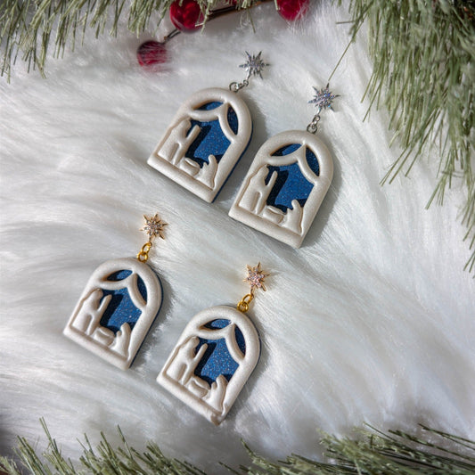 Gold and silver North Star nativity dangle earrings styled with snowy Christmas greenery