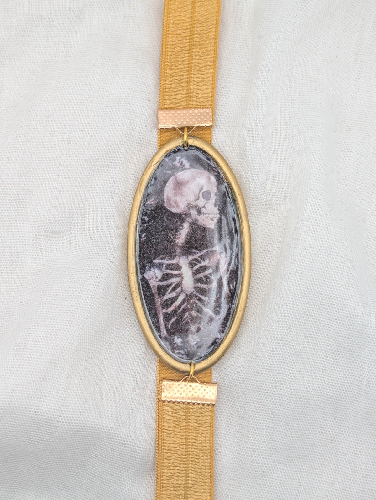 Gold framed gothic polymer clay wrap-around bookmark with a side-profile skeleton and golden brown elastic band
