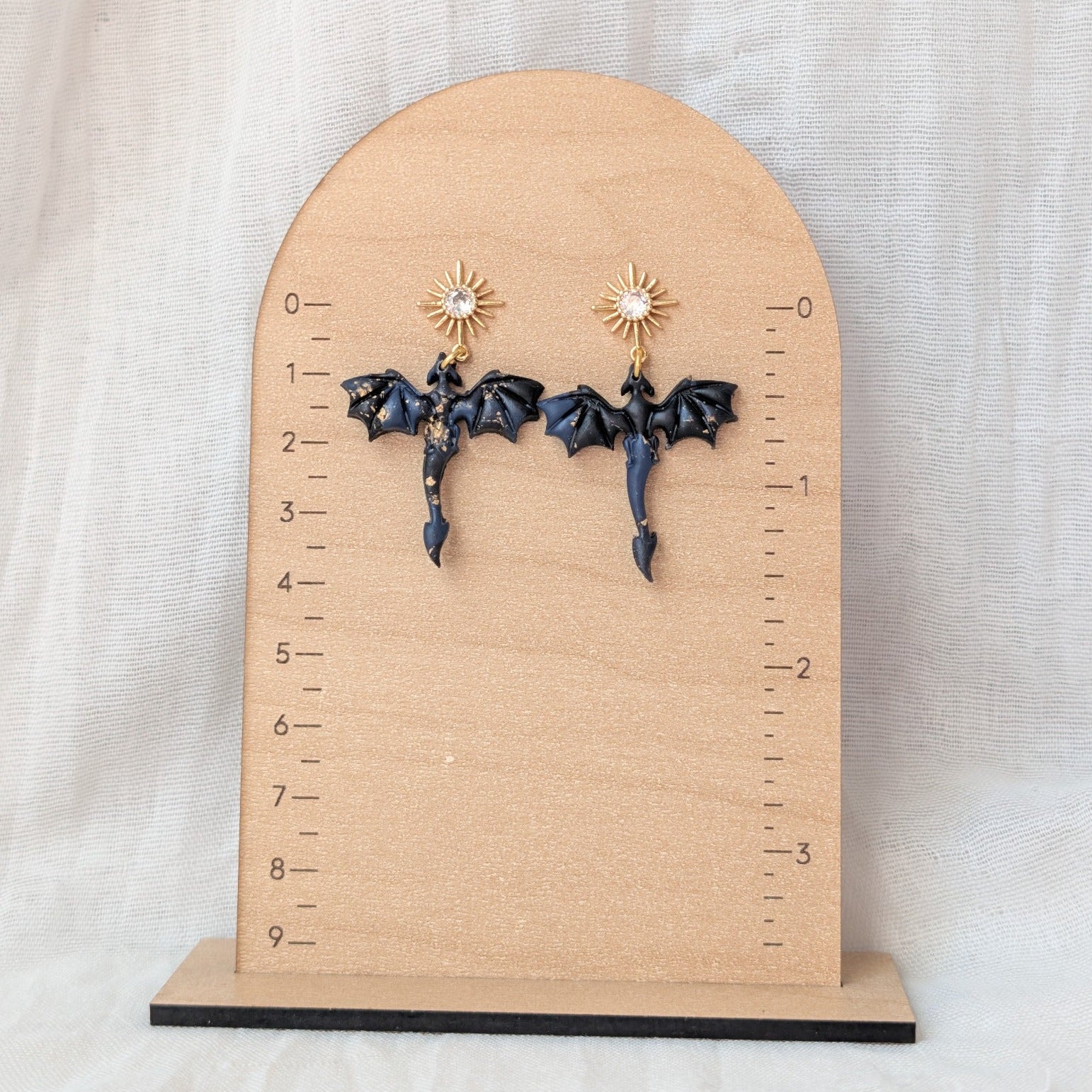 Midnight marble dragon earrings with gold starburst posts displayed beside a ruler