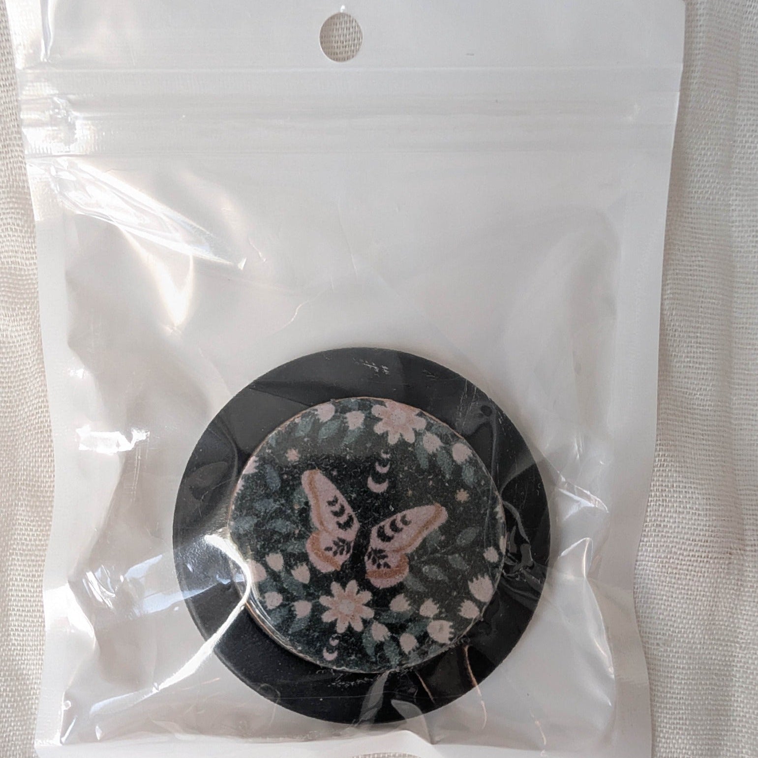 Packaged black MagSafe phone grip featuring a dusty rose moth with floral and moon phase details