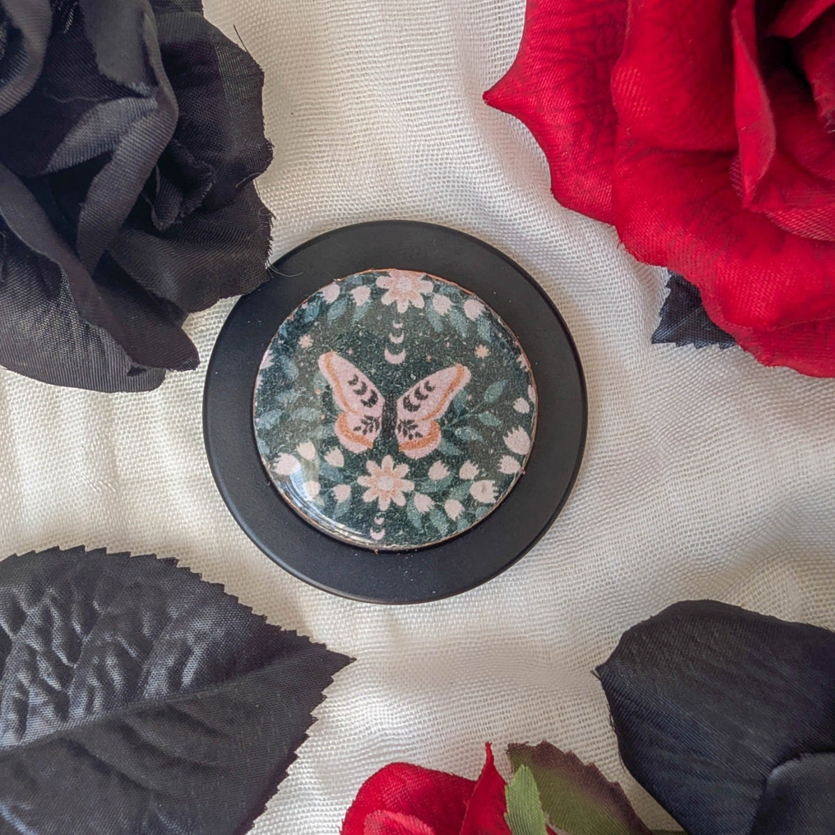 Gothic moth MagSafe phone grip with dark botanical pattern styled among red and black roses