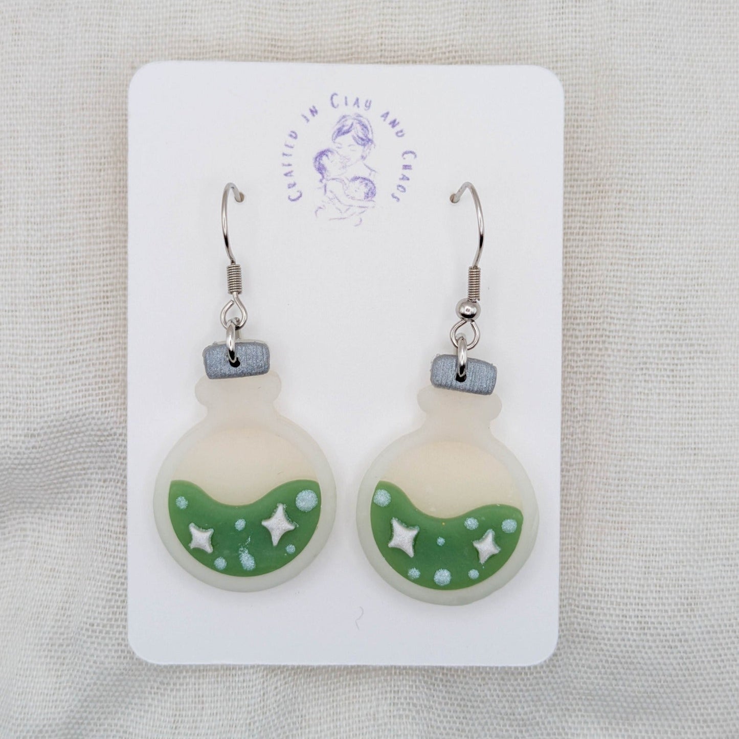 Green translucent potion bottle earrings with celestial details and surgical-grade stainless steel hooks