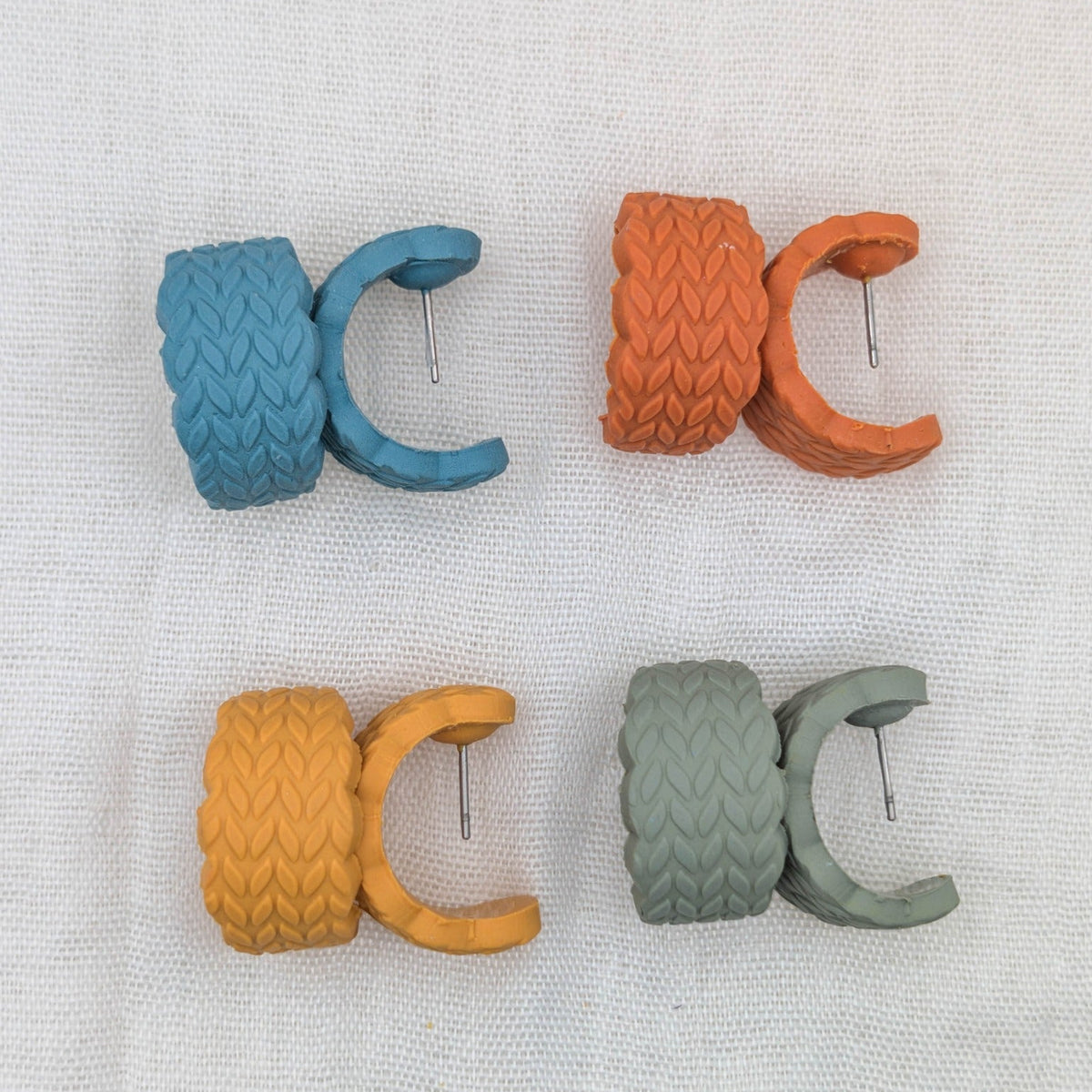 Close view of four cable-knit textured polymer clay huggie earring colors with surgical-grade stainless steel posts