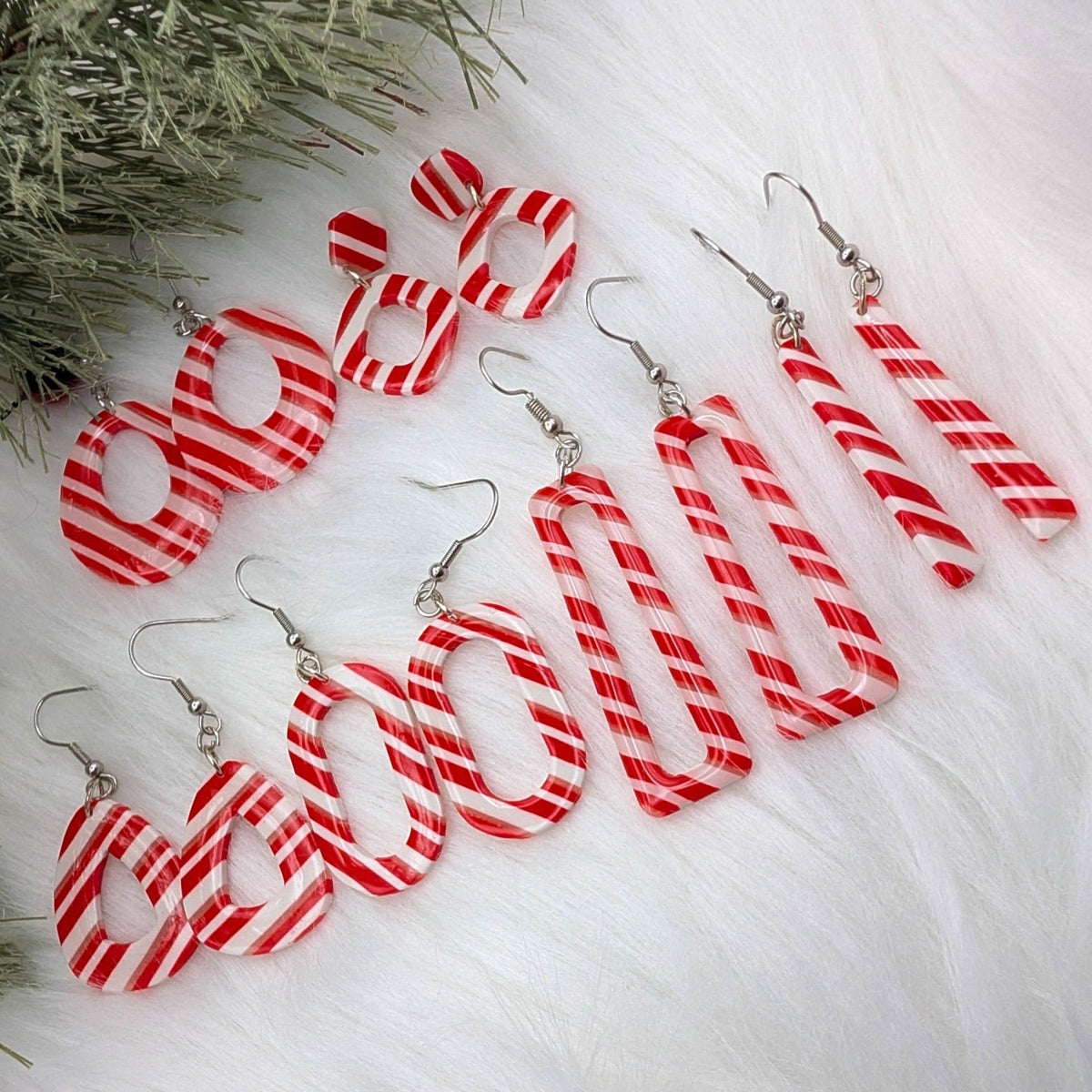 Candy Cane Lane red, white, and translucent striped polymer clay dangle earrings styled with evergreen.