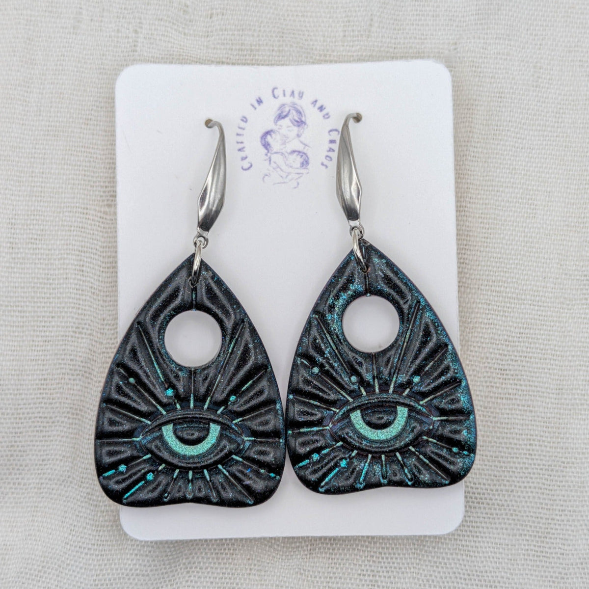 Black galaxy shimmer planchette earrings with teal all-seeing eye accents and stainless steel hooks