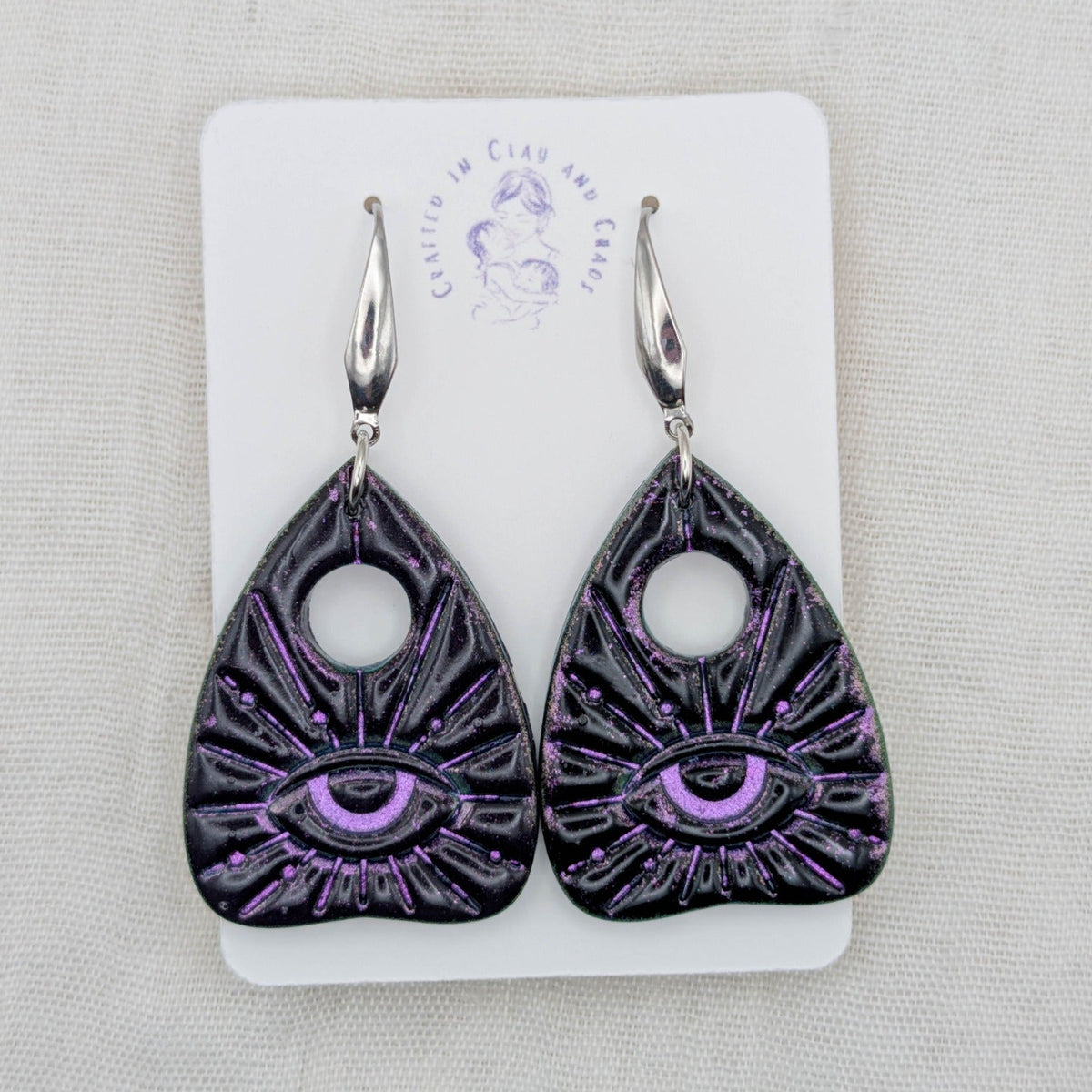 Black planchette earrings with purple shimmer, all-seeing eye details, and surgical-grade stainless steel hooks