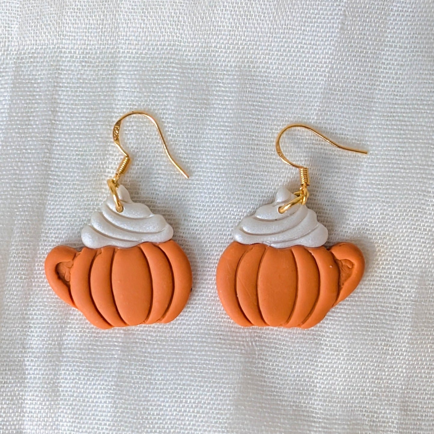 Close-up of orange pumpkin-shaped latte mug earrings with white whipped cream and gold hooks